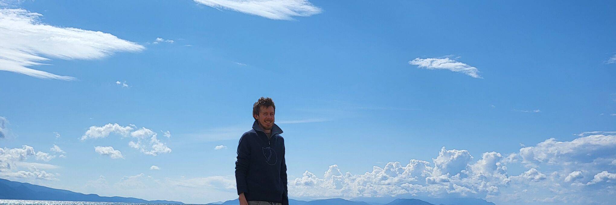 Dima steht am Strand vor blauem Himmel mit Wolken